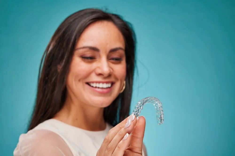 Close-up de paciente sorridente segurando alinhador transparente ClearCorrect em clínica no Anália Franco e Tatuapé.