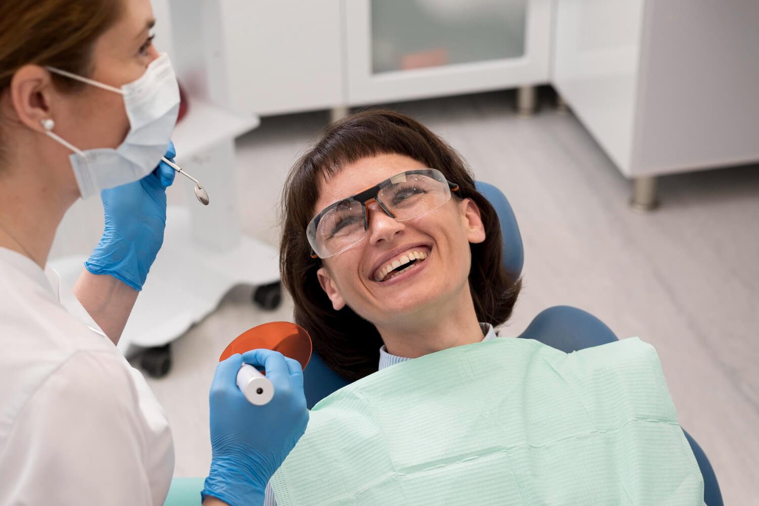 Paciente sorrindo na cadeira odontológica usando óculos de proteção durante sessão de clareamento dental no Anália Franco.