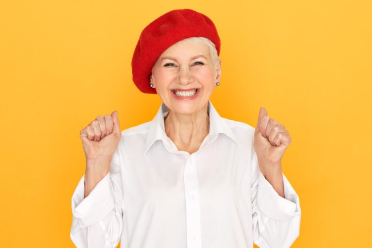 Idosa de boina vermelha sorri celebrando o rejuvenescimento facial com prótese protocolo na Felice Odontologia no Jardim Anália Franco.