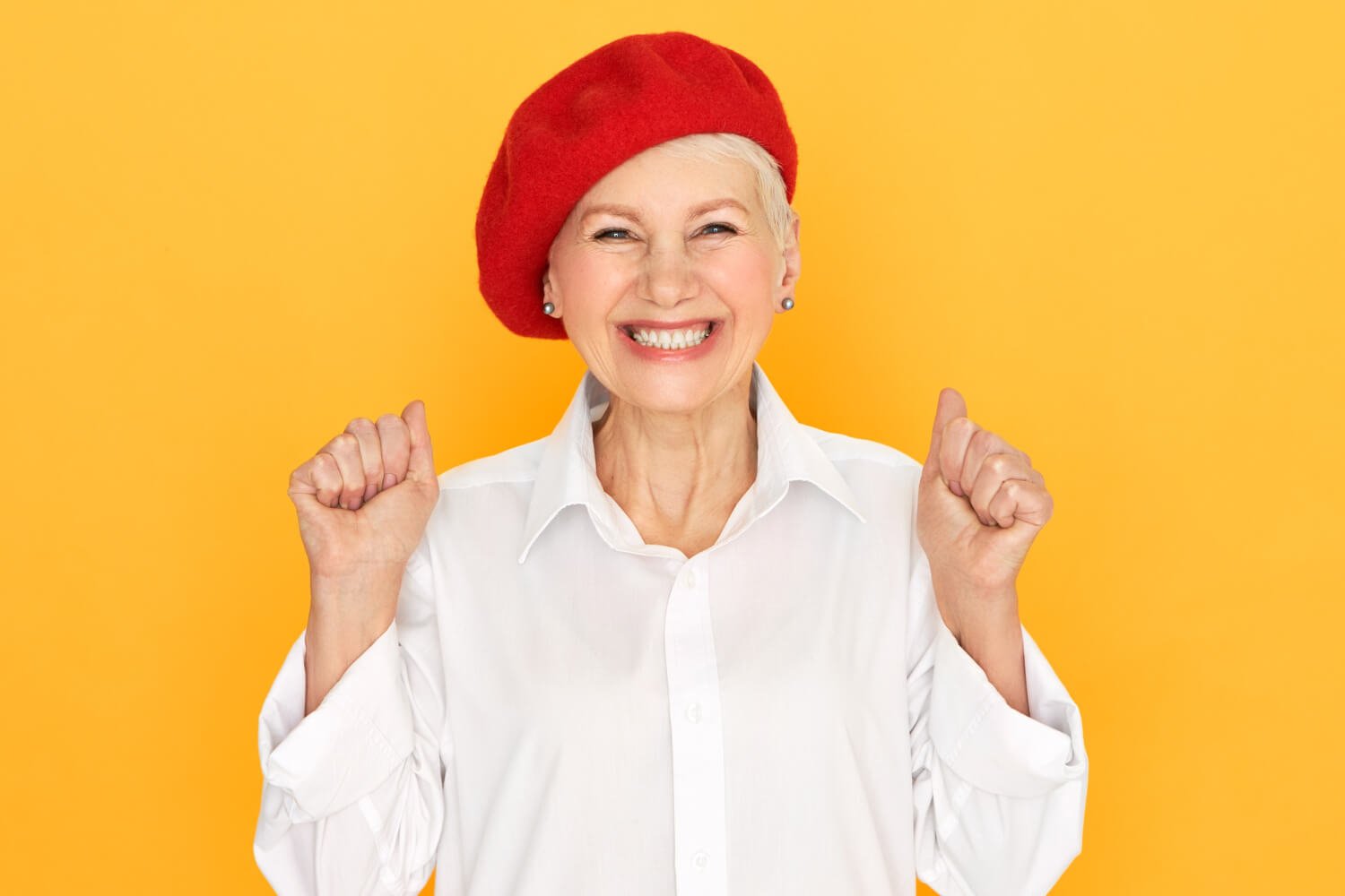 Idosa de boina vermelha sorri celebrando o rejuvenescimento facial com prótese protocolo na Felice Odontologia no Jardim Anália Franco.