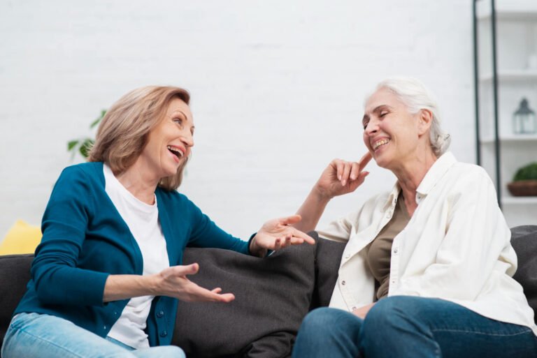 Duas mulheres da terceira idade sorrindo e conversando confortavelmente no sofá após tratamento de prótese protocolo no Jd Anália Franco.